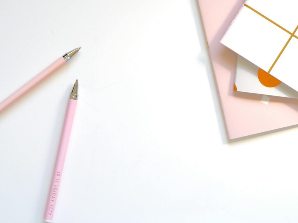 A minimalist flat lay of pink pens and pastel notebooks on a smooth white background, ideal for office and school themes.